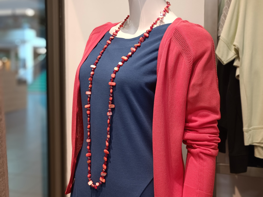 Dámské jednobarevné šaty, propínací svetřík korálové barvy, dlouhý náhrdelník z leštěných kamenů.